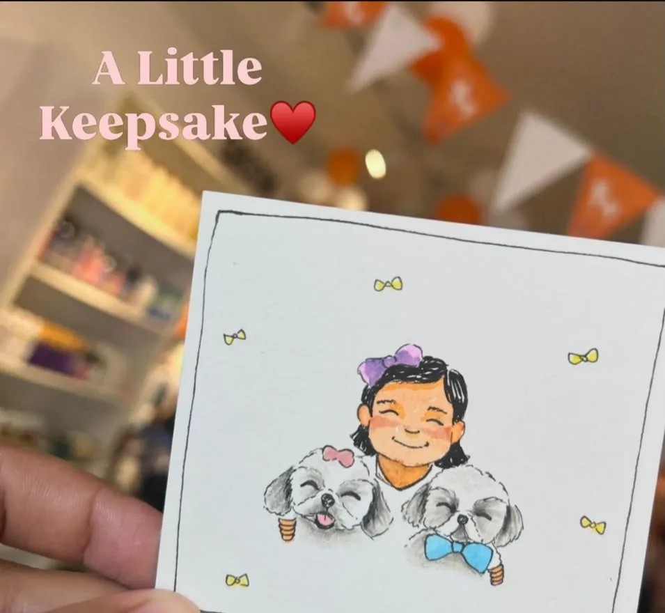 A finished caricature of two small dogs, held up in front of the stall