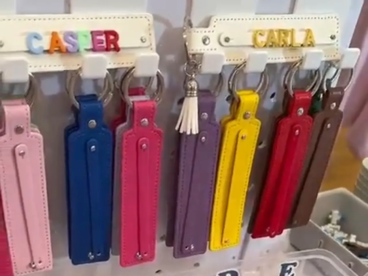 A rack of coloured leatherette keychain straps at the stall, two of them finished with beaded names